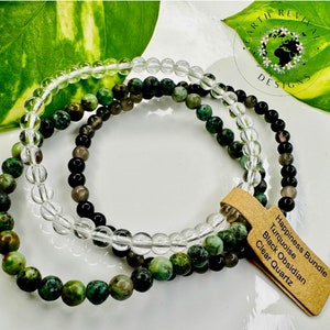 May include: Three layered bracelets made with turquoise, black obsidian, and clear quartz beads. The bracelets are labeled "Happiness Bundle, Turquoise, Black Obsidian, Clear Quartz".