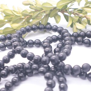 May include: A set of black beaded bracelets, made of round, smooth beads. The bracelets are arranged in a loose pile on a white background.