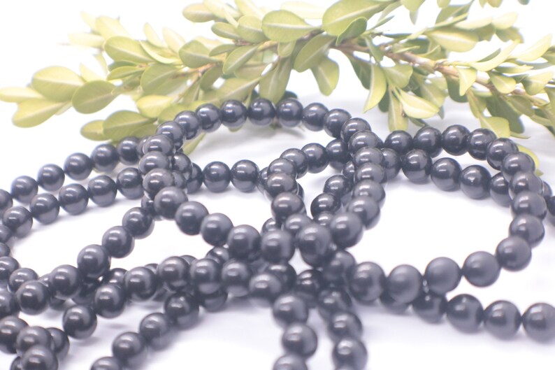 May include: A set of black beaded bracelets, made of round, smooth beads. The bracelets are arranged in a loose pile on a white background.