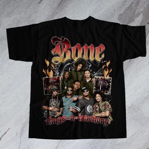 Puede incluir: Camiseta negra con un gráfico de estilo vintage del grupo de hip-hop Bone Thugs-n-Harmony. El gráfico presenta el nombre del grupo en una fuente gótica en negrita y un collage de las caras de los miembros.
