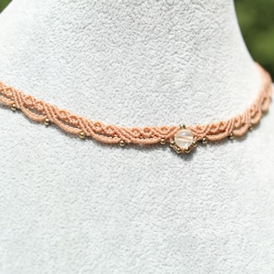 May include: A delicate peach-colored choker necklace with a small, clear gemstone pendant and gold beads.