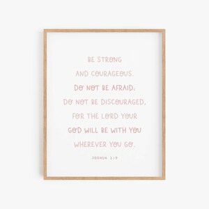 May include: A framed print with a pink inspirational quote from the Bible, Joshua 1:9. The quote reads "Be strong and courageous. Do not be afraid: Do not be discouraged, for the Lord your God will be with you wherever you go."