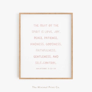May include: A printable wall art design with a light pink text quote: "The fruit of the spirit is love, joy, peace, patience, kindness, goodness, faithfulness, gentleness, and self-control. Galatians 5:22-23". The quote is framed in a light wood frame.