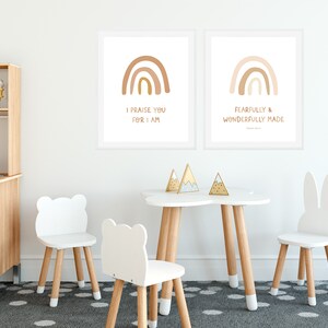 May include: Two framed prints with rainbow illustrations and inspirational quotes. The prints are hung on a white wall above a white table with four white chairs. The table is decorated with three gold mountain-shaped ornaments.