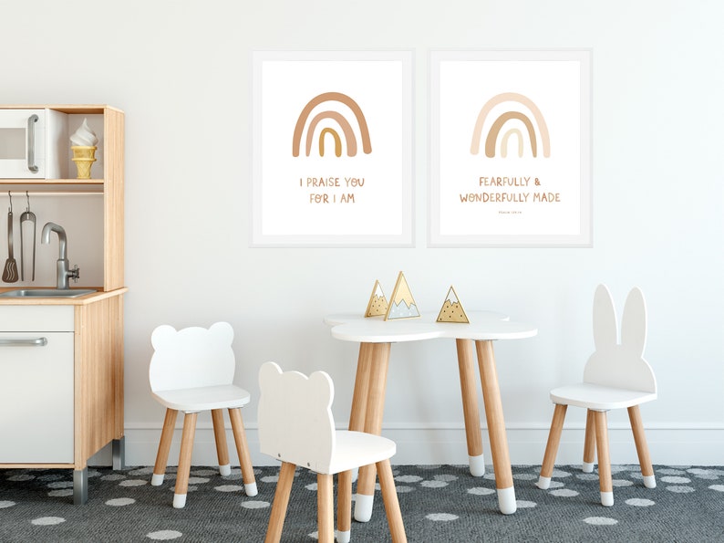 May include: Two framed prints with rainbow illustrations and inspirational quotes. The prints are hung on a white wall above a white table with four white chairs. The table is decorated with three gold mountain-shaped ornaments.