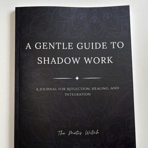 May include: A black journal titled "A Gentle Guide to Shadow Work" with white text. The cover features a decorative mandala pattern and the text "A Journal for Reflection, Healing, and Integration." The author's name, "The Metis Witch," is at the bottom.
