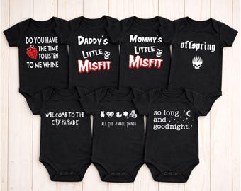May include: Black baby onesies with white text and graphics. The onesies feature phrases like "Do you have the time to listen to me whine," "Daddy's Little Misfit," and "Mommy's Little Misfit." Other onesies say "offspring," "Welcome to the Cry Parade," "All the small things," and "so long and goodnight."