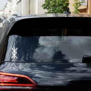 Könnte beinhalten: Ein schwarzes Auto mit einem weißen Symbol auf der Heckscheibe. Das Symbol ist ein stilisiertes geometrisches Design mit vier Punkten.
