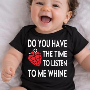 Op de afbeelding: Een zwarte babyromper met de tekst "DO YOU HAVE THE TIME TO LISTEN TO ME WHINE" in het wit. Een rode hartvormige granaat-afbeelding staat in het midden. De baby lacht.