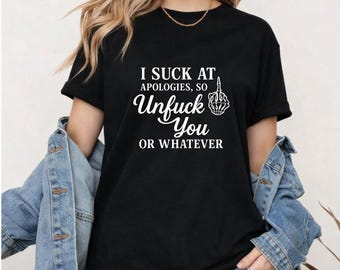 May include: Black t-shirt with the text "I SUCK AT APOLOGIES, SO Unfuck You OR WHATEVER" in white. The design includes a hand gesture. The shirt is short-sleeved.