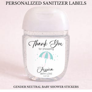 May include: A clear hand sanitiser bottle with a white lid and a label that reads "Thank You for showering" with a pink and blue umbrella design. The label also includes the name "Jessica" and the date 3.27.26. The text "PERSONALIZED SANITIZER LABELS" and "GENDER NEUTRAL BABY SHOWER STICKERS" are also visible.
