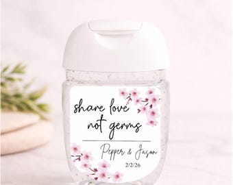 May include: A clear, travel-sized hand sanitizer bottle with a white cap. The label reads "share love not germs" with pink floral accents and personalized names and a date. The text "PERSONALIZED SANITIZER LABELS" is at the top.