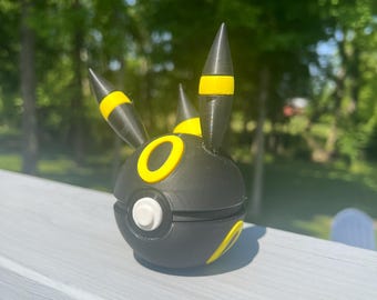 May include: A black and yellow 3D-printed Poke Ball with a white button and yellow accents. The ball has three pointed protrusions with yellow stripes. The design is a stylized representation of a popular character.