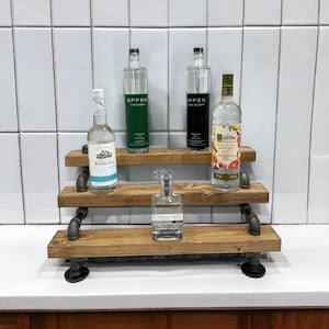 Puede incluir: Estanter&iacute;a de madera de tres niveles con soportes de tuber&iacute;a de metal negro. Las estanter&iacute;as est&aacute;n llenas de varias botellas de licor, incluyendo Effen Cucumber, Effen Black Cherry, Ketel One Grapefruit Rose, Koloa Kauai White Rum y Kohana Mea.