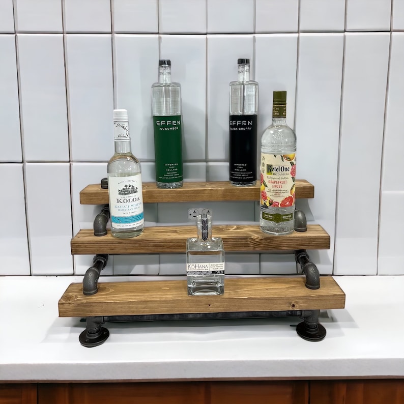 Puede incluir: Estanter&iacute;a de madera de tres niveles con soportes de tuber&iacute;a de metal negro. Las estanter&iacute;as est&aacute;n llenas de varias botellas de licor, incluyendo Effen Cucumber, Effen Black Cherry, Ketel One Grapefruit Rose, Koloa Kauai White Rum y Kohana Mea.