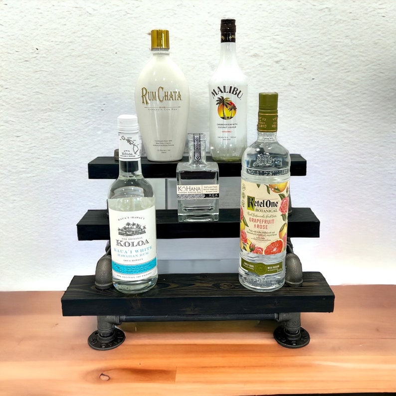 Puede incluir: Una estanter&iacute;a de metal negro de tres niveles con cinco botellas de licor. Las botellas est&aacute;n etiquetadas con "Rum Chata", "Koloa", "Kohana", "Malibu" y "Retel One Pomelo & Rosa".