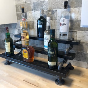 Puede incluir: Estanter&iacute;a de madera negra de tres niveles con soportes de tuber&iacute;a de metal negro. La estanter&iacute;a est&aacute; llena de varias botellas de licor, incluyendo Tito's Vodka, Crown Royal y Glenfiddich.