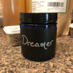 May include: A blue glass jar with a black lid and a black label that says "Dreamer" in white lettering.