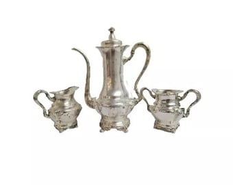 Puede incluir: Un juego de té de plata con tetera, jarra de crema y azucarero. El juego es adornado con un diseño floral.