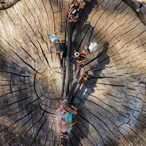 Peut inclure: Un bouquet de branches assemblées avec du fil de cuivre, orné de divers cristaux et de perles bleues et blanches en forme d'œil maléfique.