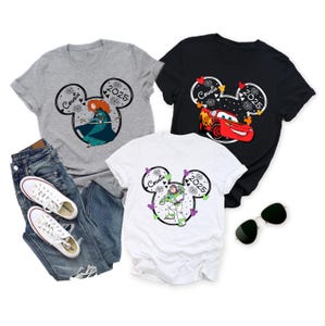 May include: Three graphic t-shirts with a Disney theme. One gray shirt features a cartoon image of Merida, the second is black with Lightning McQueen, and the third is white with Buzz Lightyear. Each shirt has "Cousin 2025" in a Mickey Mouse head design.