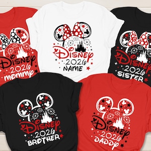 May include: A collection of Disney-themed t-shirts in red, white, and black. Each shirt features a Mickey Mouse head design with a bow, fireworks, and the text "Disney 2026" along with family member titles like "Mommy", "Sister", "Brother", and "Daddy".