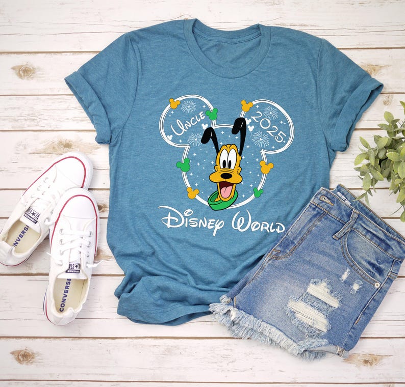 May include: A teal t-shirt with a graphic of Pluto in a Mickey Mouse outline, with the words "Uncle 2025" and "Disney World". The shirt is paired with denim shorts and white sneakers.
