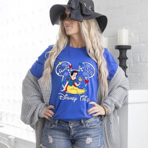 May include: Royal blue t-shirt featuring a Snow White graphic with the text "Auntie 2025 Disney Trip". The design includes a Mickey Mouse head outline with fireworks and heart accents. The shirt is a vibrant and colorful piece.