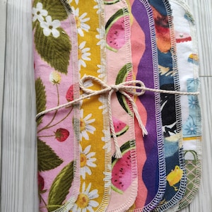 May include: A set of eight colorful reusable cloths with different patterns, including strawberries, daisies, watermelon, and a chick. The cloths are tied together with twine.