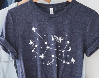 Puede incluir: Una camiseta azul marino con un gráfico blanco de la constelación de Virgo y la palabra "Virgo" en cursiva.