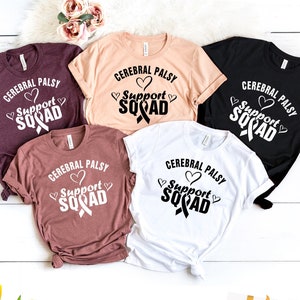 May include: Five t-shirts in different colors with the text "Cerebral Palsy Support Squad" and a black ribbon with a heart on each shirt.