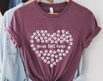 Może przedstawiać: Bordowy t-shirt z białym sercem wykonanym z odcisków łap. Wewnątrz serca znajduje się tekst "your text here".
