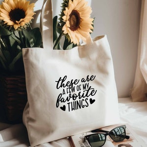 May include: A white canvas tote bag with black text that reads "These are a few of my favorite things" with two black hearts on either side of the word "things".