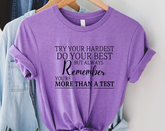 Könnte beinhalten: Lilafarbenes T-Shirt mit dem Text "Try your hardest do your best but always remember you're more than a test" in Schwarz gedruckt.