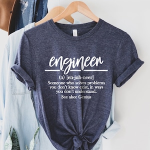 Könnte beinhalten: Ein marineblaues T-Shirt mit weißem Text, der lautet: "engineen (n) [en-juh-neer] Someone who solves problems you don't know exist, in ways you don't understand. See also: Genius"