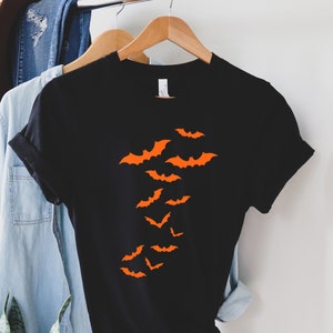 Puede incluir: Camiseta negra con un dise&ntilde;o de murci&eacute;lagos naranjas volando en un grupo.