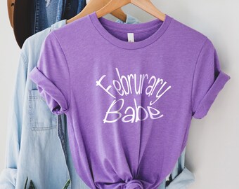 May include: Purple t-shirt with the text "February Babe" in white lettering.