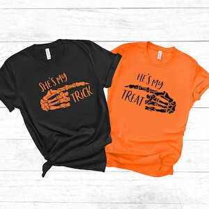 May include: Two black and orange t-shirts with a skeleton hand graphic and the text "She's my trick" and "He's my treat".