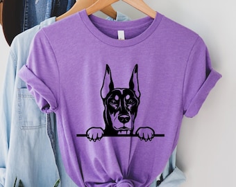 May include: A purple t-shirt with a black silhouette of a Doberman Pinscher peeking over the top edge of the shirt.