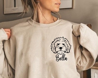 May include: A beige sweatshirt with a black outline of a dog's head and the name "Bella" printed on the front.