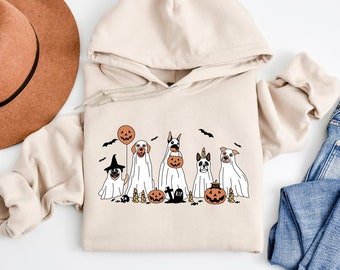 May include: A beige hoodie featuring a graphic of six dogs dressed as ghosts for Halloween. The dogs are holding pumpkins and a balloon. The graphic includes bats, a tombstone, and skulls.