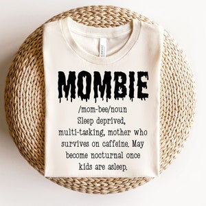 May include: A white t-shirt with black text that reads "MOMBIE /mom-bee/noun Sleep deprived, multi-tasking, mother who survives on caffeine. May become nocturnal once kids are asleep."