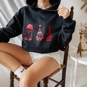 May include: Black hooded sweatshirt with a red graphic of three gnomes wearing Santa hats. The gnomes are holding gifts and the text "Believe" is printed below them.