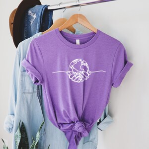 May include: Purple short-sleeved t-shirt with a white graphic of two hands holding a globe.
