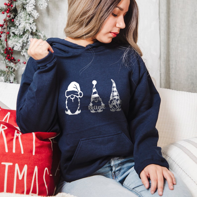 May include: A navy blue hoodie with a white design of three gnomes. The gnomes are wearing hats and have beards. The middle gnome has the word "Believe" written on its hat.