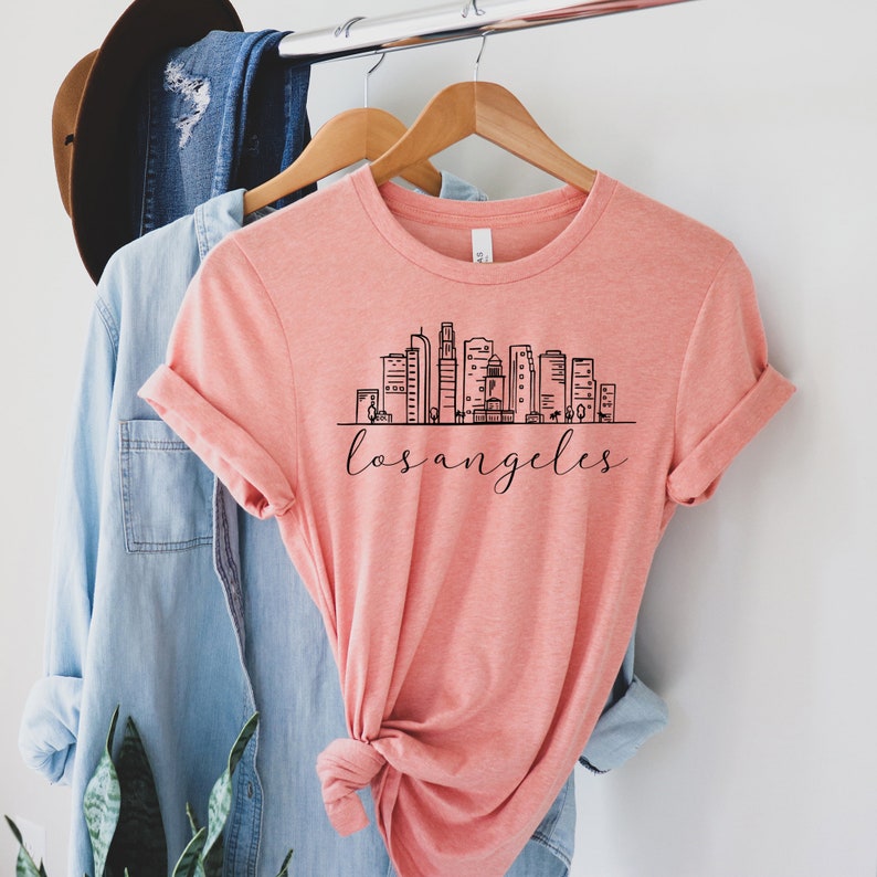 Peut inclure: Un t-shirt rose corail avec un graphique noir de l'horizon de Los Angeles et le texte "los angeles" en &eacute;criture cursive.