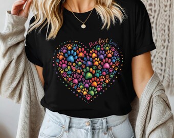 Puede incluir: Camiseta negra con un diseño en forma de corazón compuesto por huellas de patas multicolores. El corazón está lleno de huellas de patas azules, rosas, amarillas y verdes. El texto "Pawfect Love" está arqueado sobre el corazón en colores arcoíris.