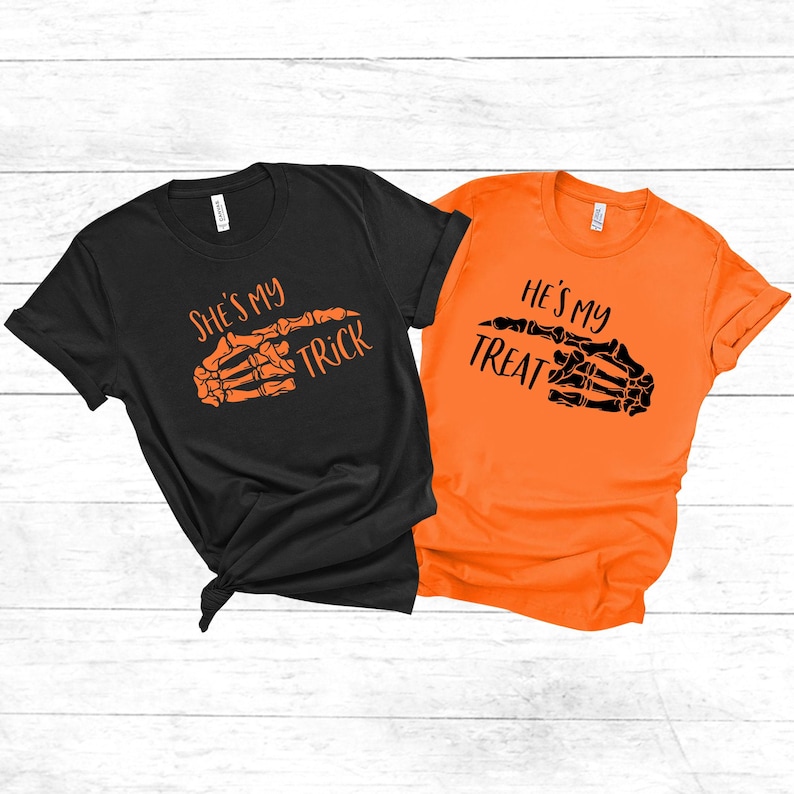 May include: Two black and orange t-shirts with a skeleton hand graphic and the text "She's my trick" and "He's my treat".