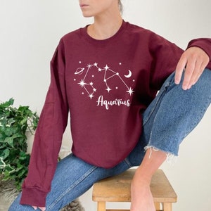 May include: A maroon sweatshirt with a white graphic of the Aquarius constellation and the word "Aquarius" printed below it.