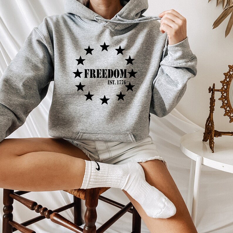 May include: A grey hooded sweatshirt with a black print of a circle of stars surrounding the words "FREEDOM EST. 1776".